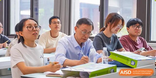 A close-up of an adult, possibly a parent or guest, taking notes during a class or presentation at Wuxi Kuangyuan Bilingual School.
