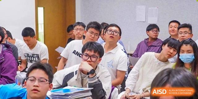 A close-up of a male student in a white shirt looking up intently while seated at his desk in a classroom at Wuxi Kuangyuan Bilingual School.