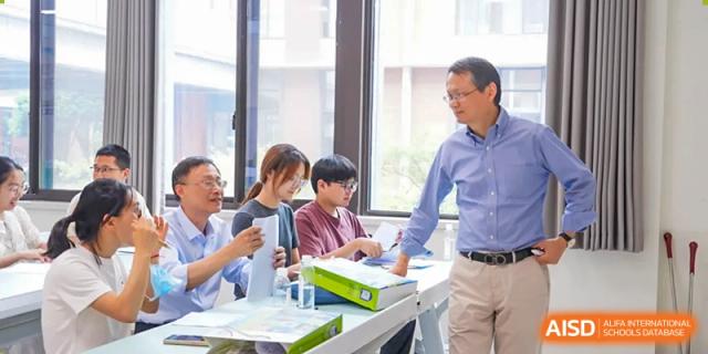 A teacher assisting a small group of students seated around a table in a bright classroom at Wuxi Kuangyuan Bilingual School.