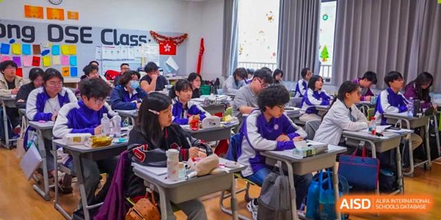 A classroom of students in uniforms engaged in an activity or lesson at their desks, with a festive decoration in the background, at Wuxi Kuangyuan Bilingual School.