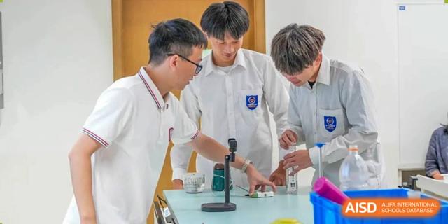 A group of male students in white uniforms collaborating on a small science experiment or demonstration on a lab table at Wuxi Kuangyuan Bilingual School.