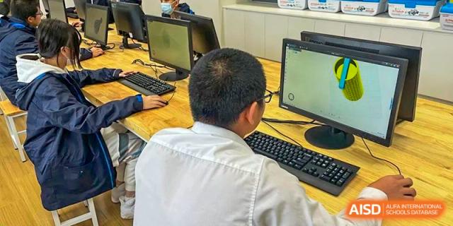 A male student working at a computer in a lab or classroom setting, viewed from behind at Wuxi Kuangyuan Bilingual School.
