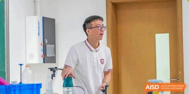 A male student in a white polo shirt actively participating in a hands-on science or classroom demonstration at Wuxi Kuangyuan Bilingual School.