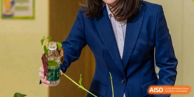 A close-up shot of an adult in a dark suit coat examining or working with a green plant or specimen in a science class at Wuxi Kuangyuan Bilingual School.