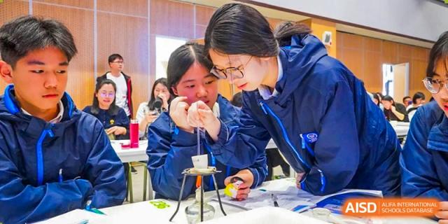 A male student in a blue jacket conducting a science experiment using a beaker heated over a lab burner at Wuxi Kuangyuan Bilingual School.