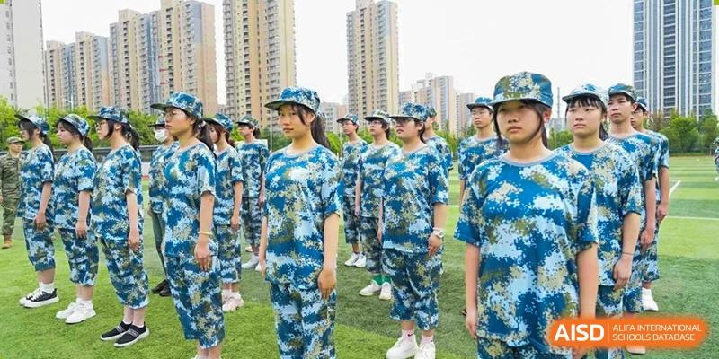 A close-up of female students in blue and white camouflage uniforms standing at attention during an outdoor training activity at Wuxi Kuangyuan Bilingual School.