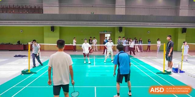 Students playing badminton in an indoor gymnasium or court with a bright green floor at Wuxi Kuangyuan Bilingual School.