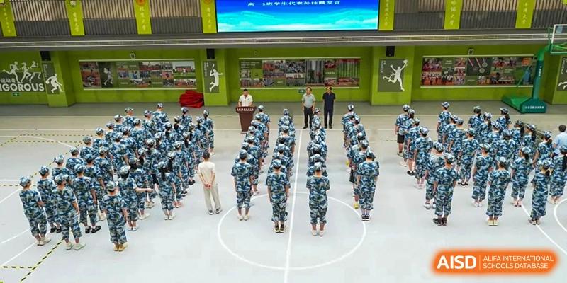 Students dressed in camouflage uniforms standing in formation on an outdoor court for a military training or assembly at Wuxi Kuangyuan Bilingual School.
