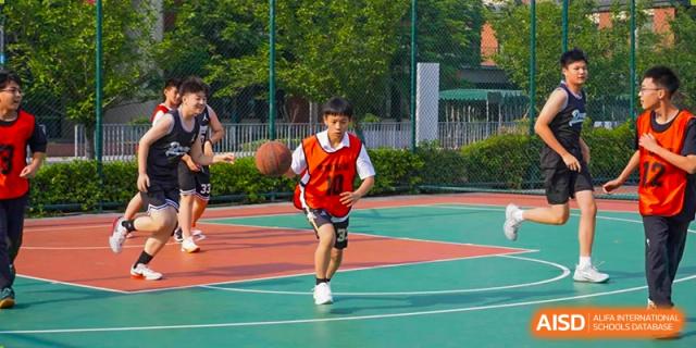 A student in a red and white jersey running with a basketball on an outdoor court at Wuxi Kuangyuan Bilingual School.