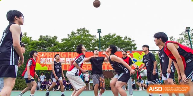 Students playing a spirited game of basketball outdoors on a court with red and black jerseys at Wuxi Kuangyuan Bilingual School.