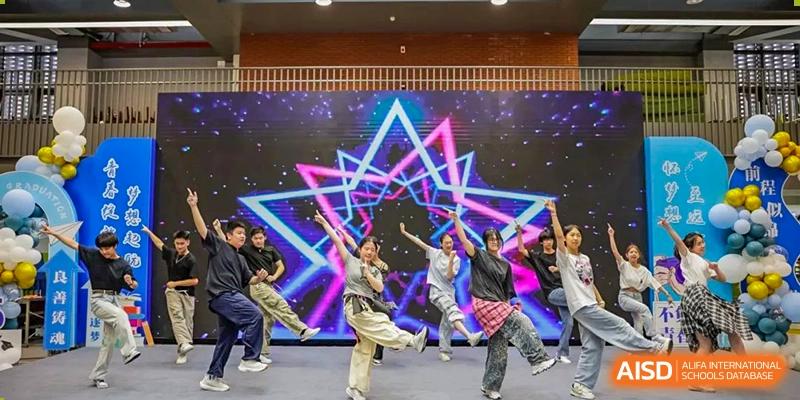 A group of students performing a dynamic dance routine on a brightly lit stage with a neon star background at Wuxi Kuangyuan Bilingual School.