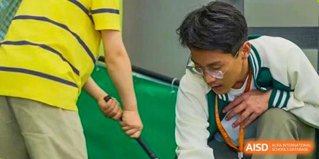 A close-up of a student in glasses focusing on a golf swing indoors at a practice facility at Wuxi Kuangyuan Bilingual School.