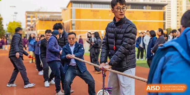 A group of adults focused on pulling the rope during a tug-of-war competition on a sports field at Wuxi Kuangyuan Bilingual School.