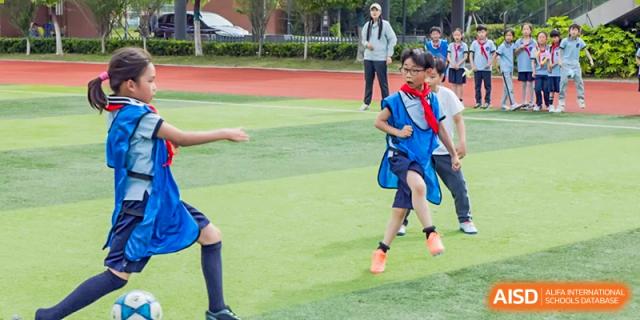 Young students playing a game of soccer or participating in a sports drill on a grass field at Wuxi Kuangyuan Bilingual School.
