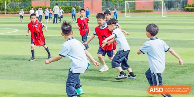 Elementary students running after a soccer ball during a lively sports activity on a turf field at Wuxi Kuangyuan Bilingual School.