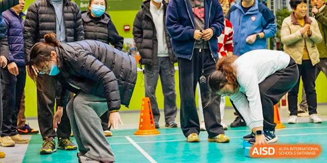 Adults observing or participating in an outdoor sports activity with orange cones set up on the field at Wuxi Kuangyuan Bilingual School.