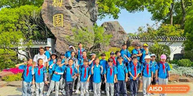 A large group of students in blue school uniforms and red scarves posing for a group picture in a rocky, outdoor natural setting at Wuxi Kuangyuan Bilingual School.