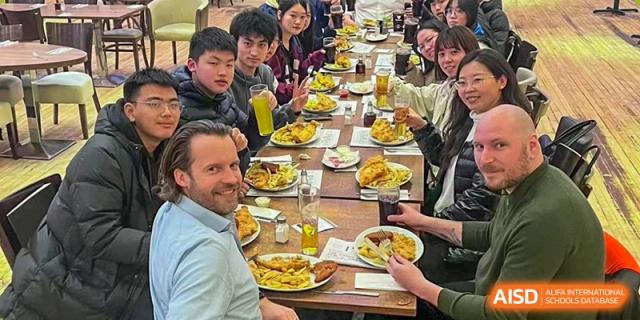 A group of students and a foreign teacher enjoying a communal meal together at a long table at Wuxi Kuangyuan Bilingual School.
