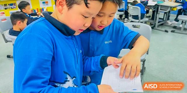 Two young students in blue uniforms reading a paper together at Wuxi United International School.
