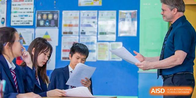 A male student reviewing papers or documents, likely an academic task at Wuxi United International School.
