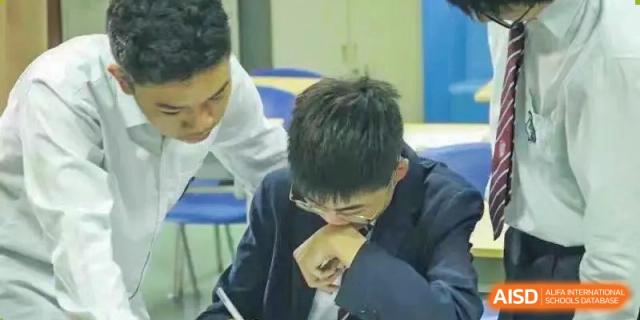 A male student in glasses looking down at his hand while concentrating at Wuxi United International School.