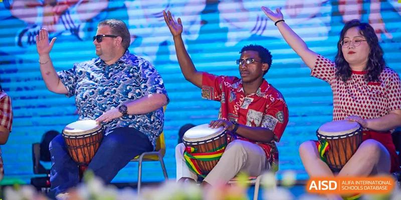 A man playing a djembe drum enthusiastically during an outdoor cultural event at Wuxi United International School.