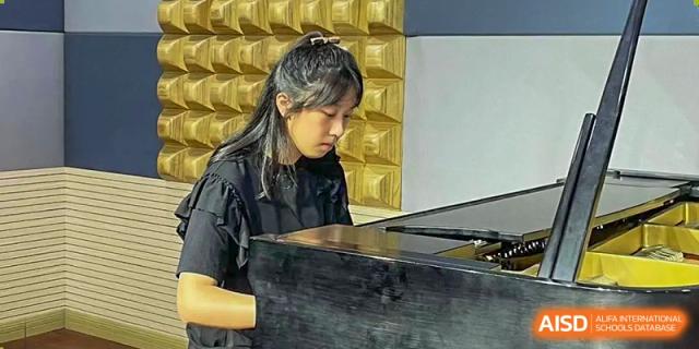 Female student in a black outfit concentrating while playing the piano at Wuxi United International School.