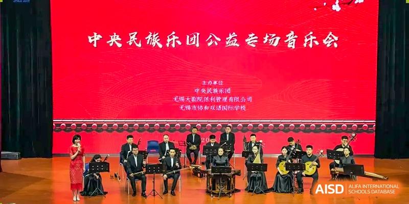 Folk music ensemble seated in front of a red screen displaying Chinese text at Wuxi United International School.