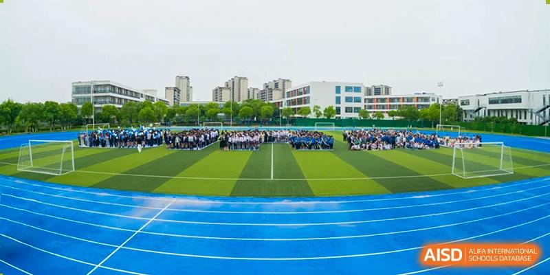 Students gathered on the green sports field next to the blue running track at Wuxi United International School.