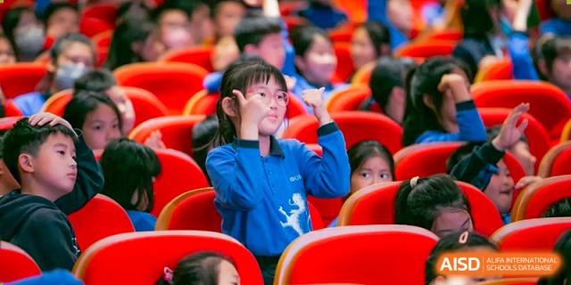 Young student in a blue shirt making a hand gesture while watching an event at Wuxi United International School.