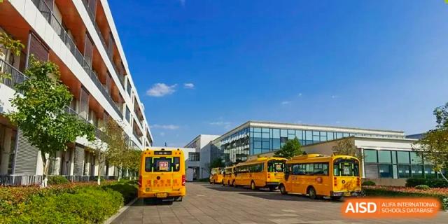 Exterior view of the modern school building and yellow buses parked at Wuxi United International School.