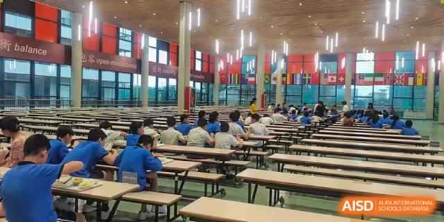 Students from Wuxi United International School sitting at long tables in a bright, large cafeteria during a mealtime.