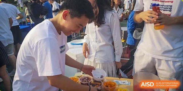 Students or staff from Wuxi United International School serving food from bowls and preparing snacks at an outdoor or school event.