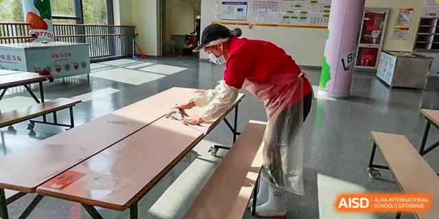 A person from Wuxi United International School cleaning or setting up a long cafeteria table with benches.