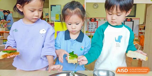 A young female student from Wuxi United International School focused on a hands-on activity, placing a green item on a small piece of food.