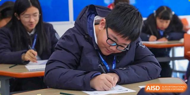 A male student from Wycombe Abbey School Nanjing writing in a notebook in a classroom.