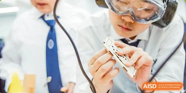A student from Wycombe Abbey School Nanjing holding up a white rectangular object with a teacher in the background.