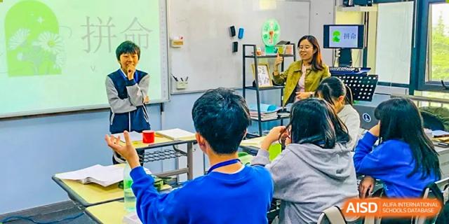 A Xi'an International School teacher giving a lesson to a class of students seated at desks in a bright classroom setting.