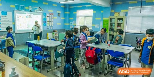 Xi'an International School students working in small groups at tables in a brightly lit classroom with blue and green furniture.