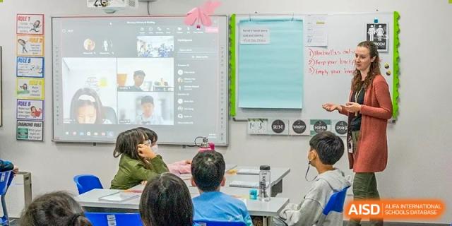 A Xi'an International School classroom setting where students are participating in a hybrid or online lesson displayed on a large screen.