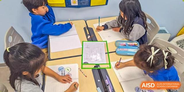 A close-up of a Xi'an International School student's hands writing on a worksheet at a classroom desk.