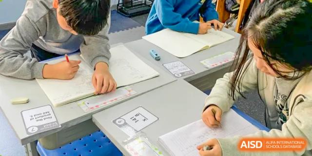 Two Xi'an International School students working on a paper-based assignment together at a gray desk.
