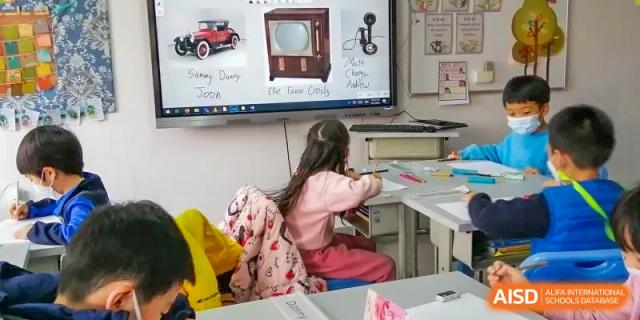 A female Xi'an International School student with long hair works on a school assignment at a desk with a pink backpack nearby.