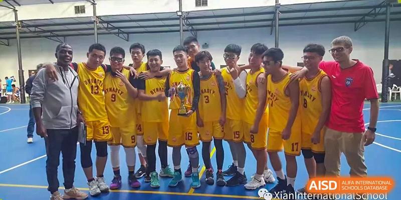 A championship basketball team from Xi'an International School, wearing yellow jerseys, posing together with a trophy on the court.