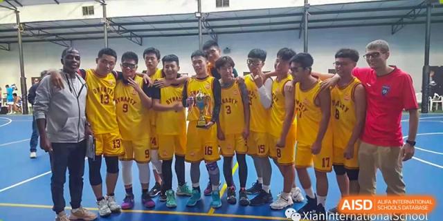 A championship basketball team from Xi'an International School, wearing yellow jerseys, posing together with a trophy on the court.