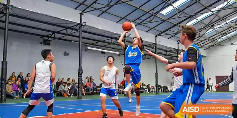 An action shot of two Xi'an International School students playing basketball, with one player in a blue jersey shooting a jump shot.