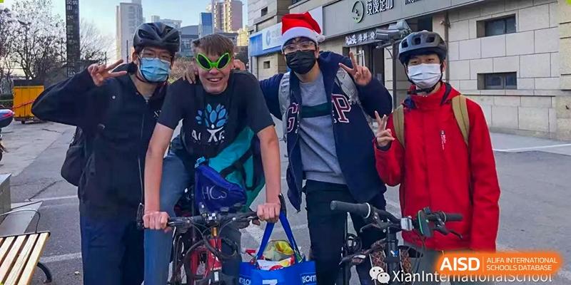 Two Xi'an International School students posing outdoors, one wearing a Santa hat and a mask, and the other wearing green novelty alien sunglasses.
