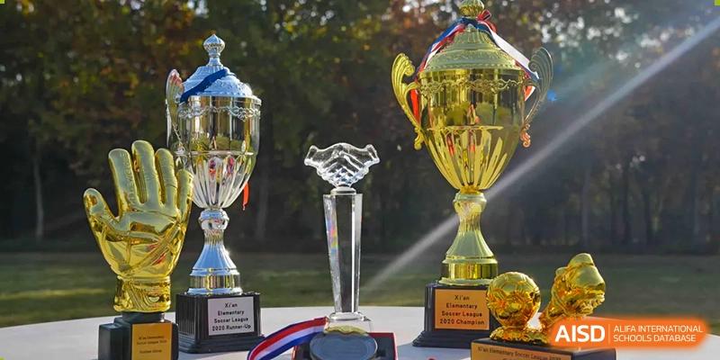 A display of several silver and gold trophies and awards, including one with a handshake design, representing an event at Xi'an International School.