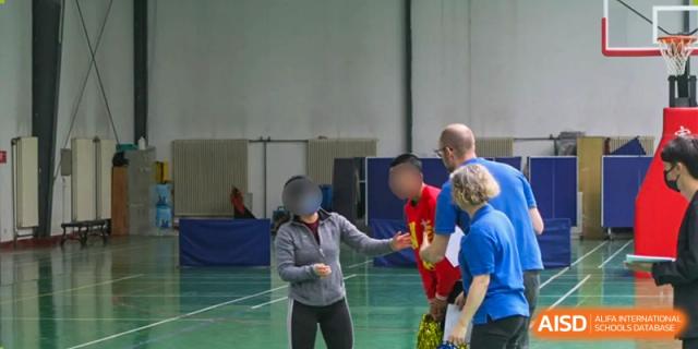 An adult and a student from Xi'an International School participating in an indoor sports activity, possibly badminton or a similar racket sport.