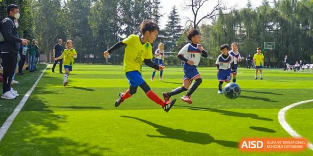 Two Xi'an International School students in brightly colored jerseys running intensely across a green sports field during an outdoor competition.